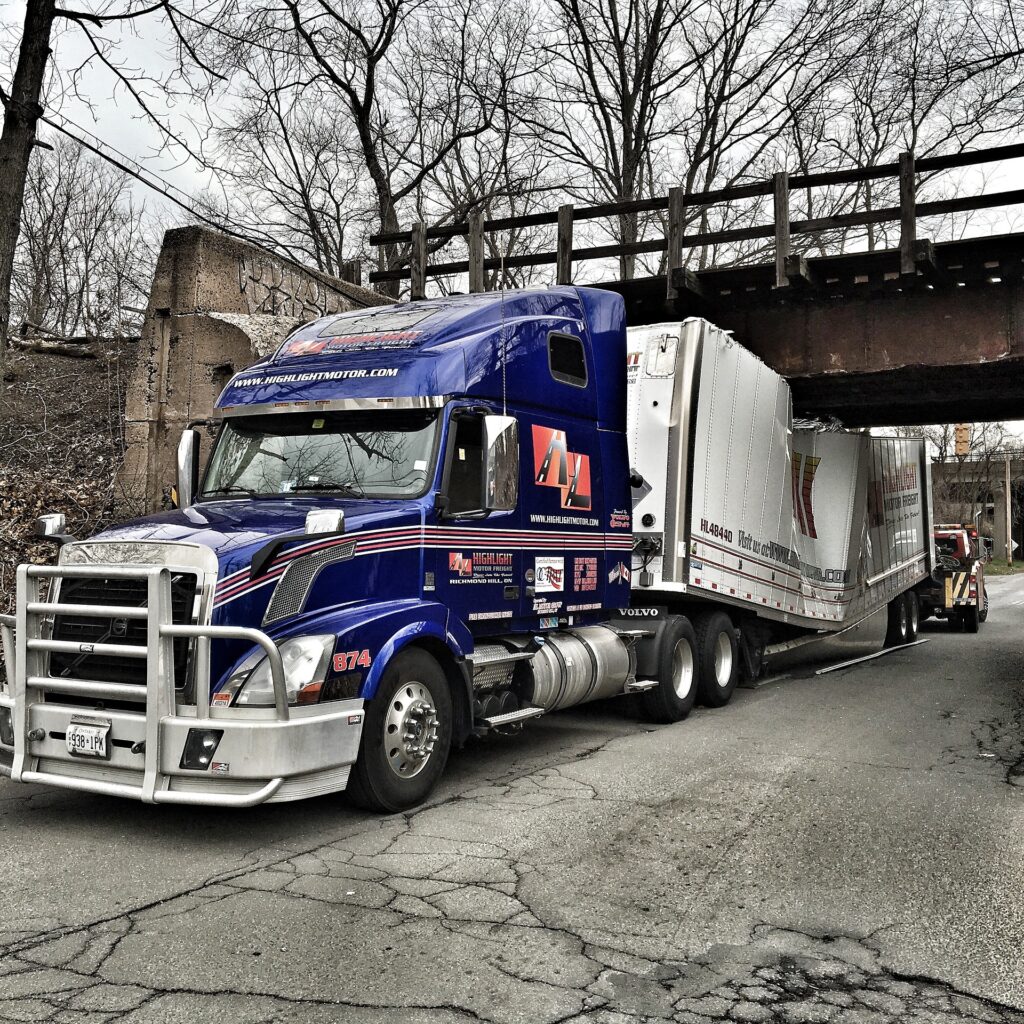 A huge blue truck stuck under the bridge