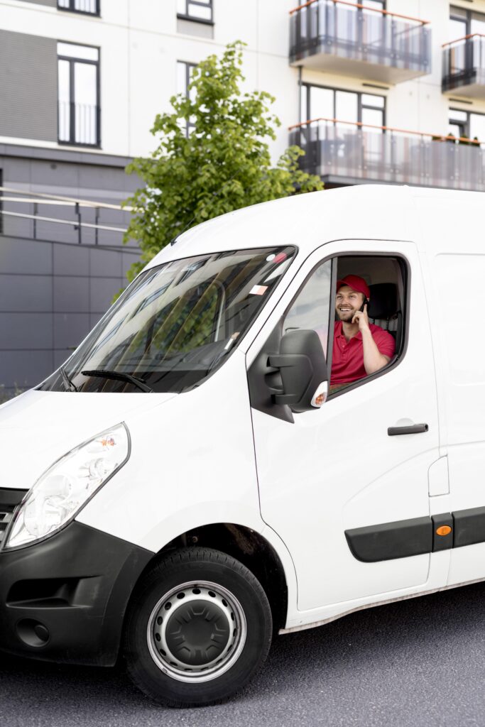 A man wearing a red cap and uniform driving a white delivery service truck